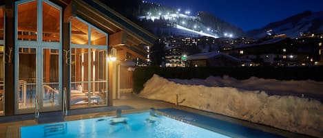 A hotel with a pool, glass doors, and a view of a snow-covered mountain at night.
