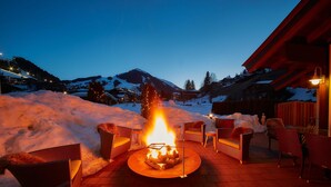 Feuerstelle mit Stühlen, Schnee und einem Berg im Hintergrund.