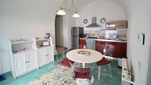 Une cuisine de taille réduite avec des meubles blancs, une table à manger entourée de chaises transparentes et un tapis aux motifs colorés.