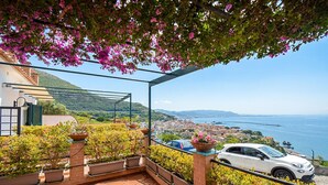Un balcon orné de plantes en pot, une voiture blanche et une vue sur une ville côtière.