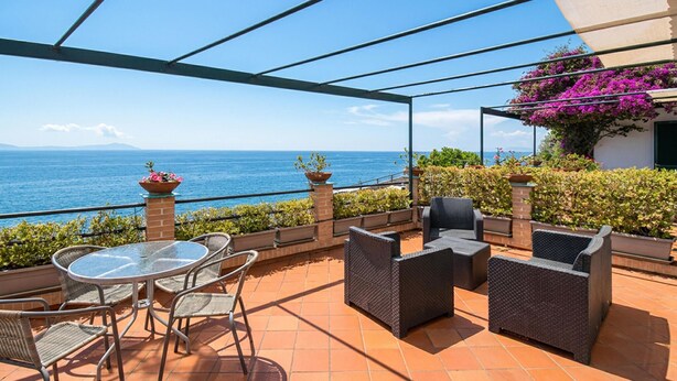 Une terrasse extérieure avec une table en verre et des chaises en osier, offrant une vue sur la mer.
