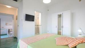 Une chambre à coucher avec un lit, une télévision, une armoire et une salle de bain visible à travers une porte ouverte.
