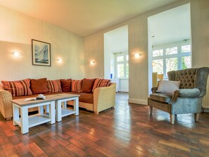 A spacious living room with a wooden floor, a large sofa, a smaller armchair, and a coffee table. - Villa Waldburg Whg. VW-04. - Villa Waldburg Whg. 04 (Kühlungsborn)