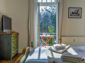 A bedroom with a bed, a television on a dresser, a balcony with a table and chairs, and a framed picture on the wall. - Villa Waldburg Whg. VW-04. - Villa Waldburg Whg. 04 (Kühlungsborn)