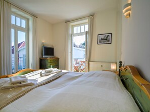 A bedroom with a bed, a television on a wooden cabinet, a framed picture on the wall, and a balcony with chairs. - Villa Waldburg Whg. VW-04. - Villa Waldburg Whg. 04 (Kühlungsborn)