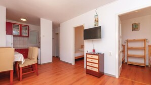 A room with a wooden floor, a bed, a TV mounted on the wall, a small table with a chair, and a kitchen area with red cabinets. - Amazing apartment in Jadrija with WiFi (Jadrija)