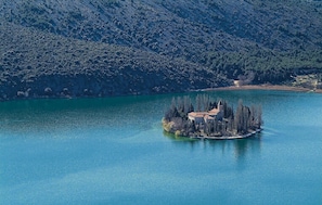 An island with a building surrounded by trees, located in a large body of water with mountains in the background. - Amazing apartment in Jadrija with WiFi (Jadrija)