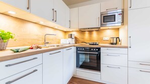 A modern kitchen with white cabinets, a built-in oven, a microwave, and a wooden countertop. - Apartment 07 - Haus Windrose: 2 Vacation Rentals in the Heart of Binz (Binz)