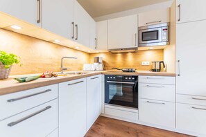 A modern kitchen with white cabinets, a built-in oven, a microwave, and a wooden countertop.