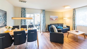 A modern living room with a dining area, featuring a sofa, coffee table, and dining table with chairs. - Apartment 07 - Haus Windrose: 2 Vacation Rentals in the Heart of Binz (Binz)