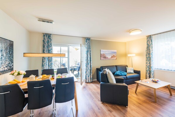 Ein modernes Wohnzimmer mit Essbereich, ausgestattet mit einer Couch, Couchtisch und Esstisch mit Stühlen.