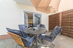 Eine Terrasse mit einem runden Tisch, vier Stühlen, einem Sonnenschirm und einem Holzzaun.