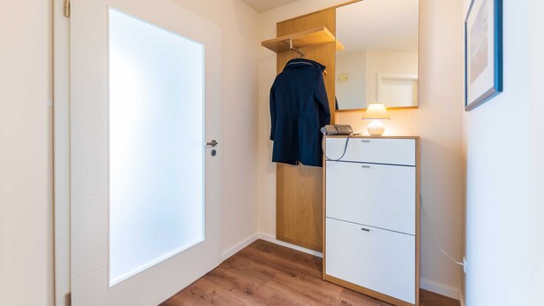 A hallway with a wooden wardrobe, a mirror, and a white door. - Apartment 07 - Haus Windrose: 2 Vacation Rentals in the Heart of Binz (Binz)