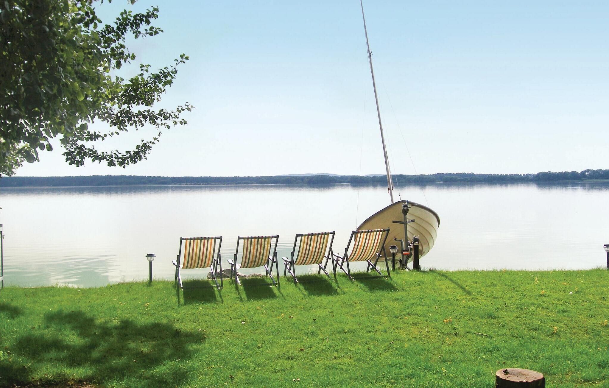A boat docked at a calm lake with four striped chairs and a fishing rod.