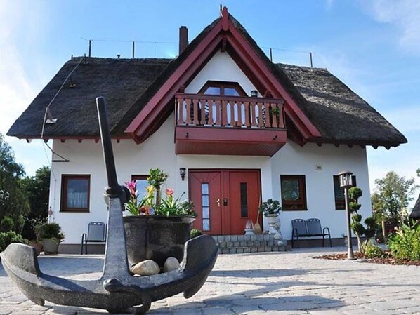 A two-story house with a red door, a balcony, and a thatched roof. - Apartment 2 - FeWo Zum Anker near Warnemünde - Object 27276 (Rostock)