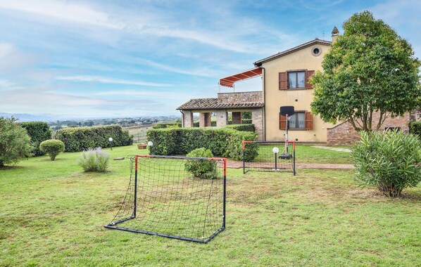 Una casa con cancha de tenis en el patio trasero, rodeada de setos cuidados y vistas al campo.