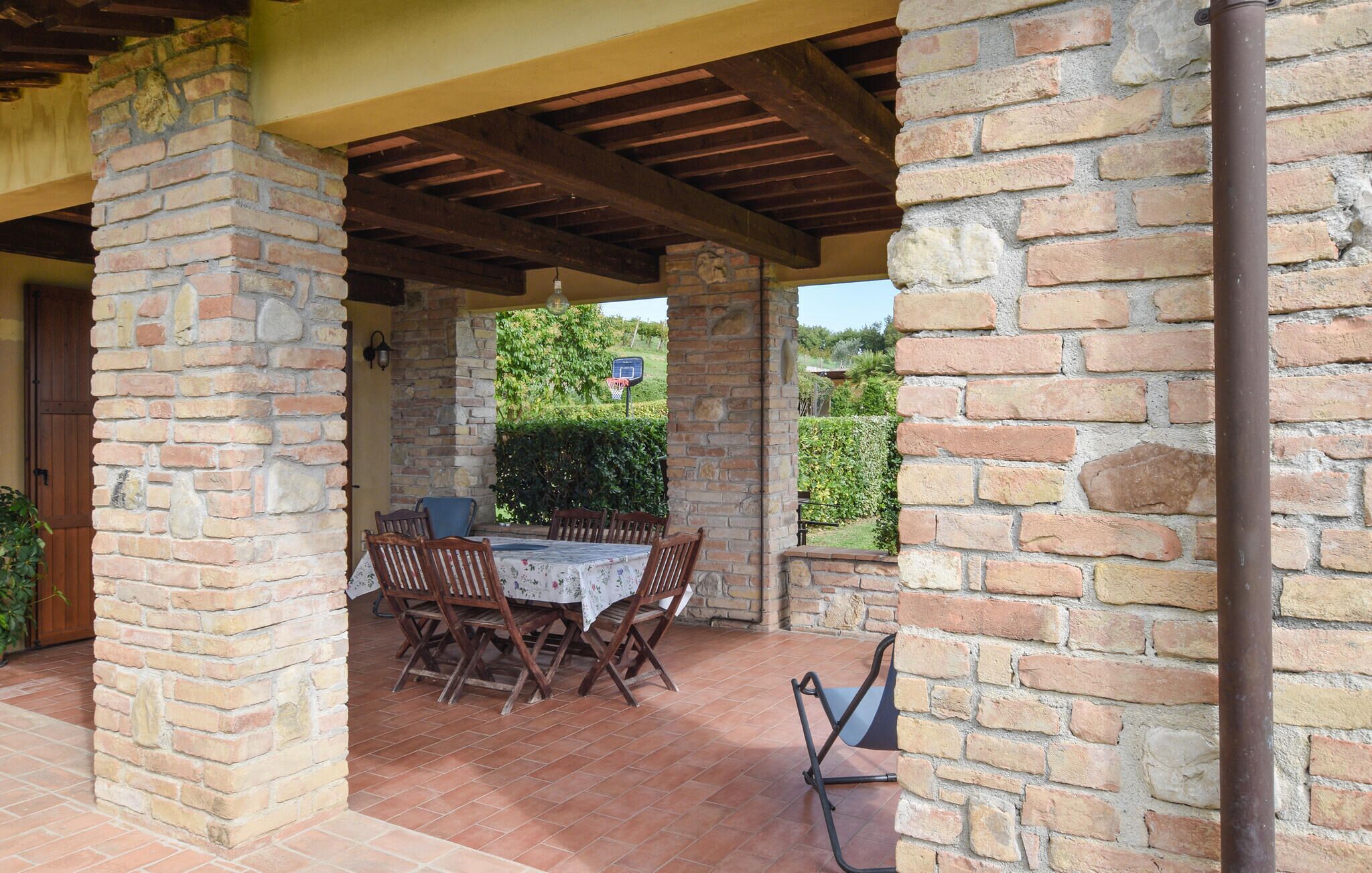 Un patio al aire libre con una mesa y sillas de ladrillo, rodeado de muros de piedra y un techo de madera.