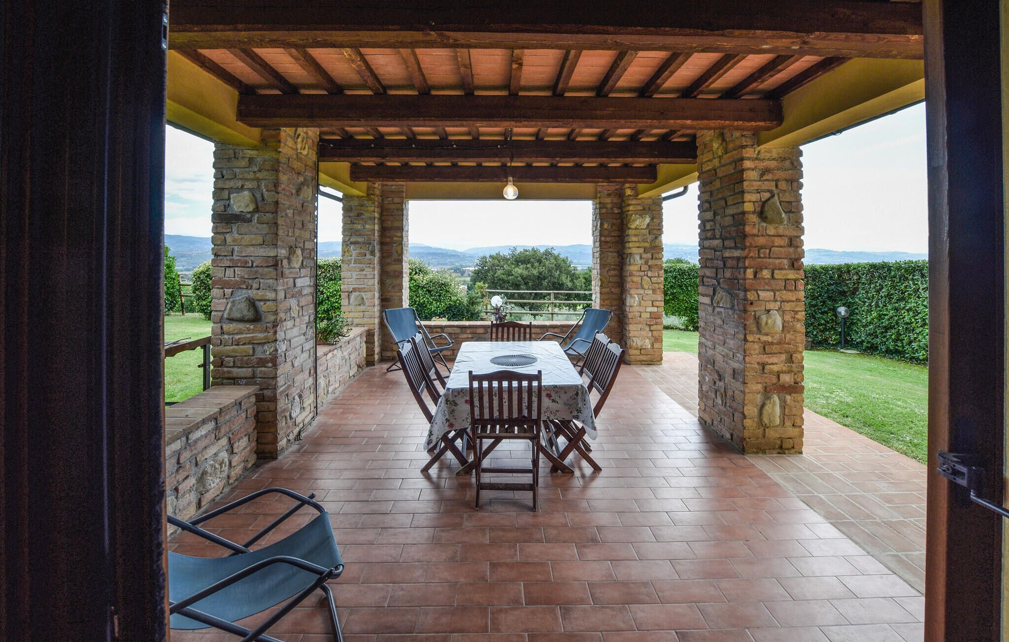 Um alpendre coberto com mesa e cadeiras, pilares de pedra e vista para o campo.