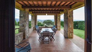 Un patio cubierto con una mesa y sillas, pilares de piedra y vistas al campo.