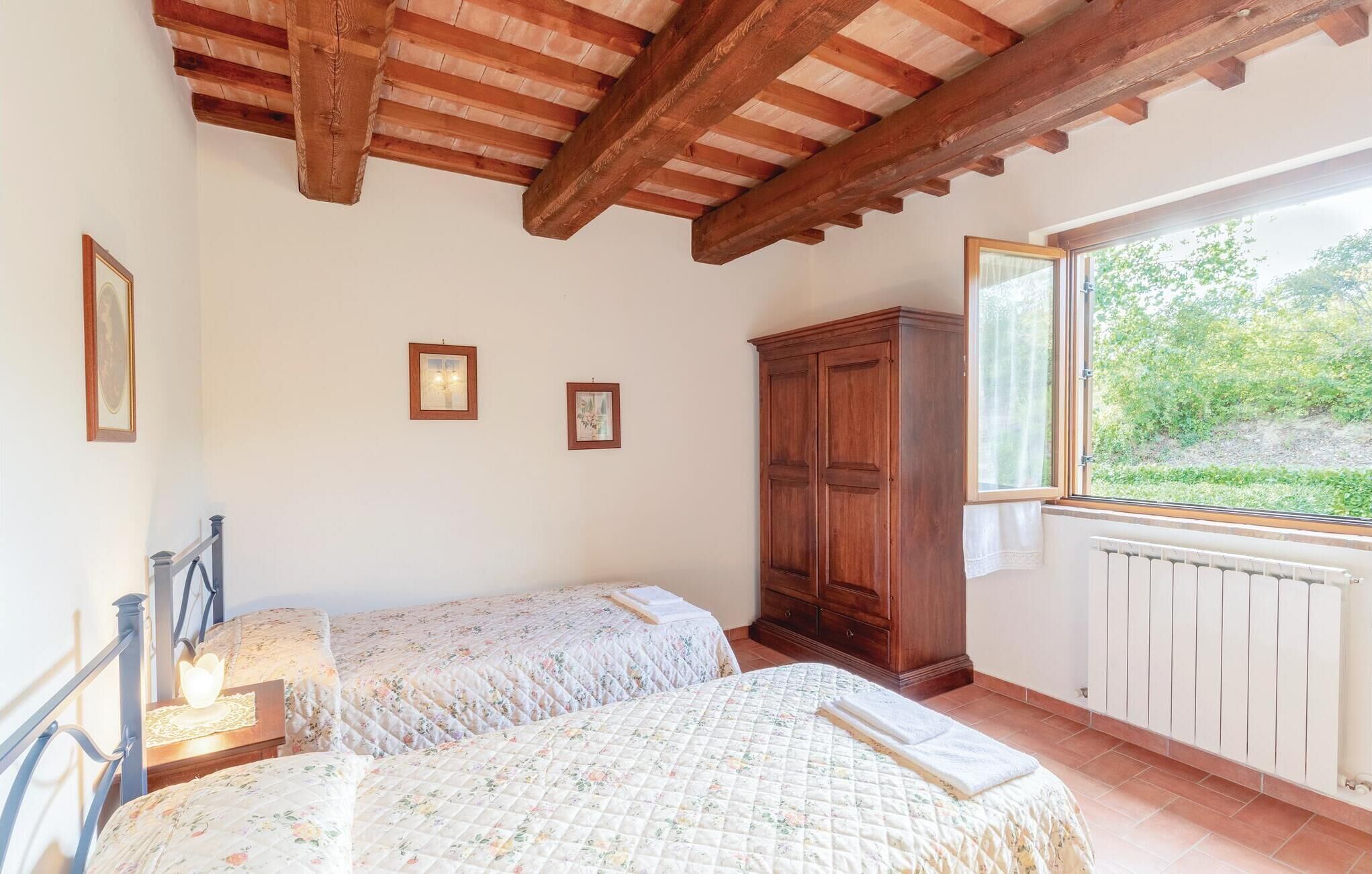 Une chambre avec deux lits, des poutres apparentes en bois au plafond, une grande fenêtre et un radiateur.