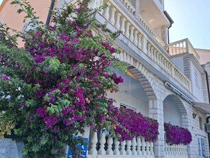 A building with a balcony and arches, with purple flowers hanging from the railing. - Studio with air conditioning and terrace (Dramalj)