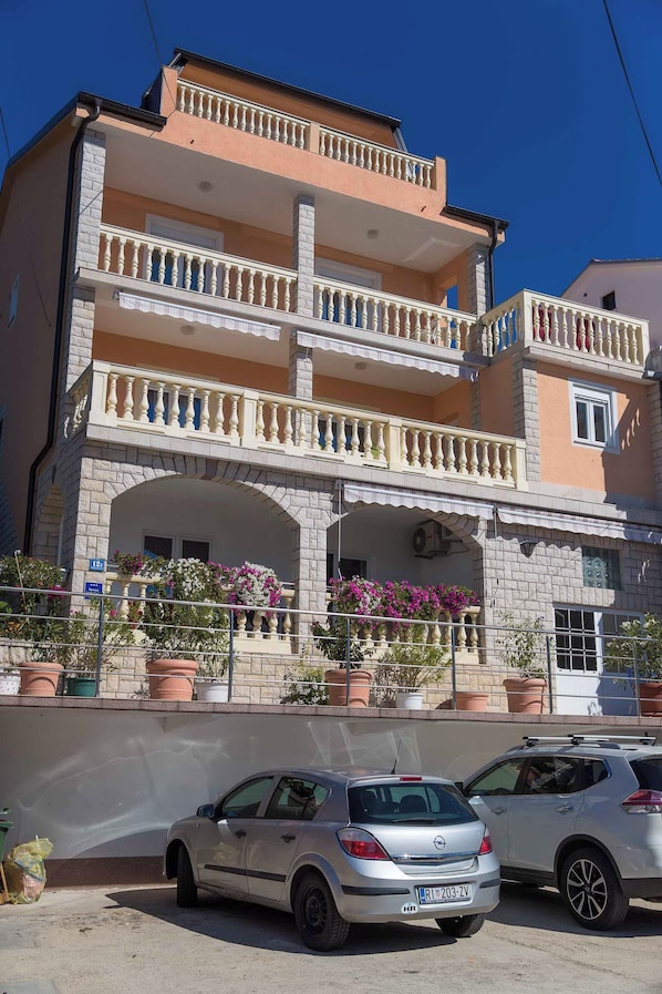 A multi-story building with balconies, potted plants, and parked cars.