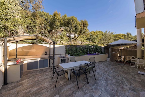 Un patio al aire libre con mesa y sillas, una zona de barbacoa y un área de estar techada.