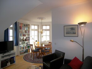 A living room with a television, bookshelves, a dining area with chairs, and a floor lamp.
