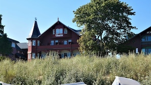 Een groot, rood gebouw met de naam 'Vineta' op de gevel, omringd door hoog gras en bomen.