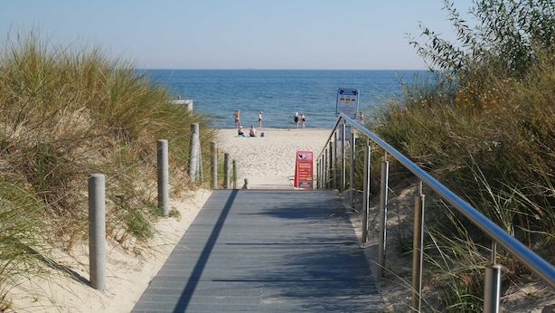 Een pad dat naar een strand leidt, met een metalen hek aan één kant en zand aan de andere kant.