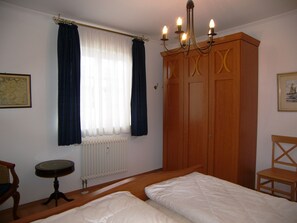 Un dormitorio con dos camas, un armario de madera, un radiador y una mesita.