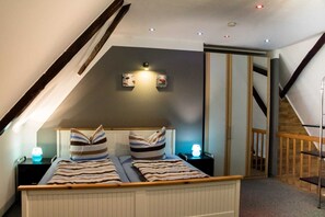 Une chambre avec un plafond en pente, un lit avec une literie à rayures, deux lampes de chevet et un luminaire fixé au mur.
