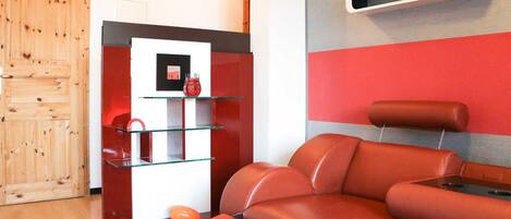 A modern living room with a red leather sofa, a glass coffee table, and a wooden door.
