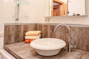 Une salle de bain avec un lavabo blanc, un lambris en bois, une étagère en verre et un miroir.