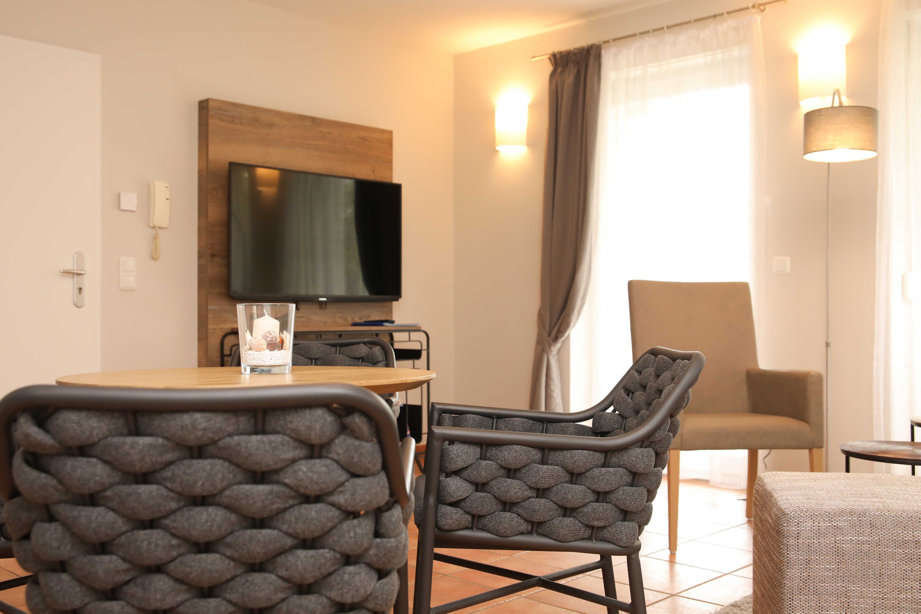 A modern dining area with a wooden table, two upholstered chairs, a television mounted on the wall, and a lamp.