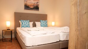 Una cama doble con ropa blanca y almohadas estampadas, una mesita de noche con lámpara, y un cuadro en la pared.
