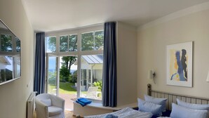 Een hotelkamer met een groot raam, een bed met blauw beddengoed, een witte stoel en een schilderij aan de muur.