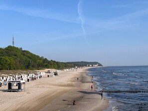 Een strand met een zandstrand, enkele mensen die wandelen en een verre heuvel met gebouwen.
