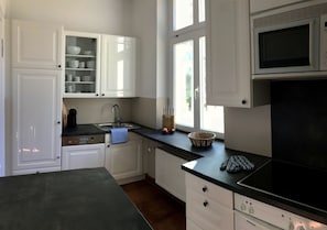 Een keuken met witte kastjes, een zwart aanrecht, een magnetron, een fornuis en een raam.