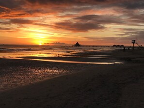 Une plage avec un coucher de soleil, une jetée et un poste de surveillance des sauveteurs.