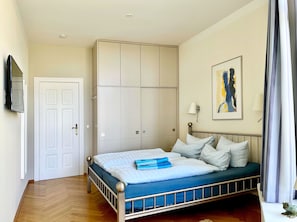 Een slaapkamer met een bed, een kledingkast, een televisietoestel en een schilderij aan de muur.