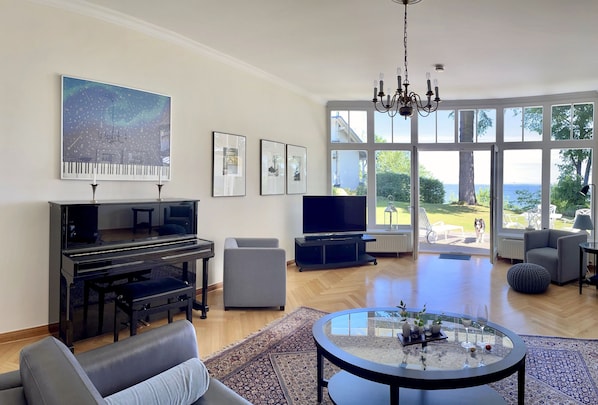 Ein Wohnzimmer mit Klavier, Fernseher und einem großen Fenster mit Blick ins Freie.