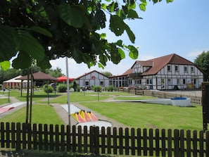 A park with a playground, a building with a red roof, and a wooden fence. - Vacation home 131 Lederstrumpf 66sqm up to 6 persons with pet - Holiday home (Hollern-Twielenfleth)