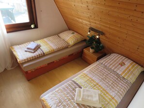 Ein kleiner, gemütlicher Raum mit zwei Betten, Holzwänden, einem Fenster mit Blume und einem Nachttisch mit Lampe.