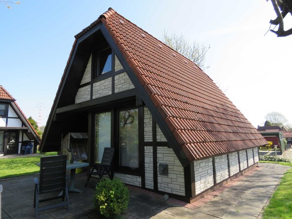A two-story house with a steeply pitched roof, large windows, and a small patio area with outdoor furniture. - Vacation home 131 Lederstrumpf 66sqm up to 6 persons with pet - Holiday home (Hollern-Twielenfleth)