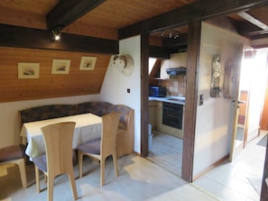 A cozy room with a wooden ceiling, a dining table with chairs, a kitchen area with a microwave, and a small oven. - Vacation home 131 Lederstrumpf 66sqm up to 6 persons with pet - Holiday home (Hollern-Twielenfleth)