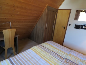 A bedroom with a sloped ceiling, wooden wardrobe, and a bed with striped bedding. - Vacation home 131 Lederstrumpf 66sqm up to 6 persons with pet - Holiday home (Hollern-Twielenfleth)