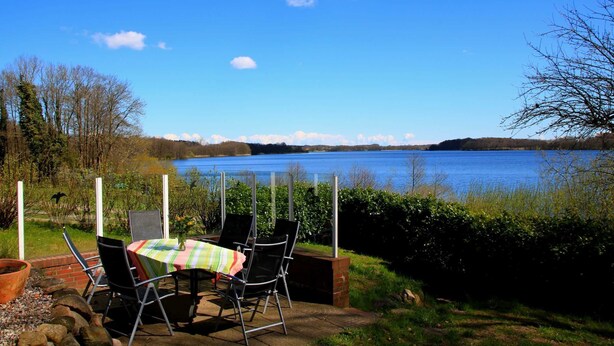 A patio with a table and chairs overlooking a lake. - RED Holiday home at the Bistensee - Holiday home Frick (Alt Duvenstedt)