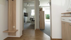 A hallway with wooden flooring, a kitchen area with cabinets and a dining table, and a view of the outdoors. - Reriker Straße 06b Whg. RER6b-2 .. - Reriker Str. 6b Whg. RER6b-02 (Kühlungsborn)