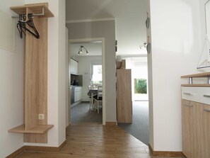 A hallway with wooden flooring, a kitchen area with cabinets and a dining table, and a view of the outdoors. - Reriker Straße 06b Whg. RER6b-2 .. - Reriker Str. 6b Whg. RER6b-02 (Kühlungsborn)